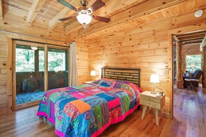 A wooden cabin bedroom with a large bed, two bedside lamps, and a ceiling fan.