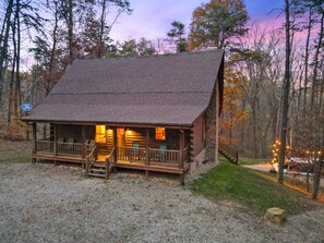 A rustic cabin with a porch, wooden steps, and a gravel driveway.