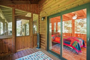 A wooden cabin with a large sliding glass door leading to a bedroom with a colorful bedspread.