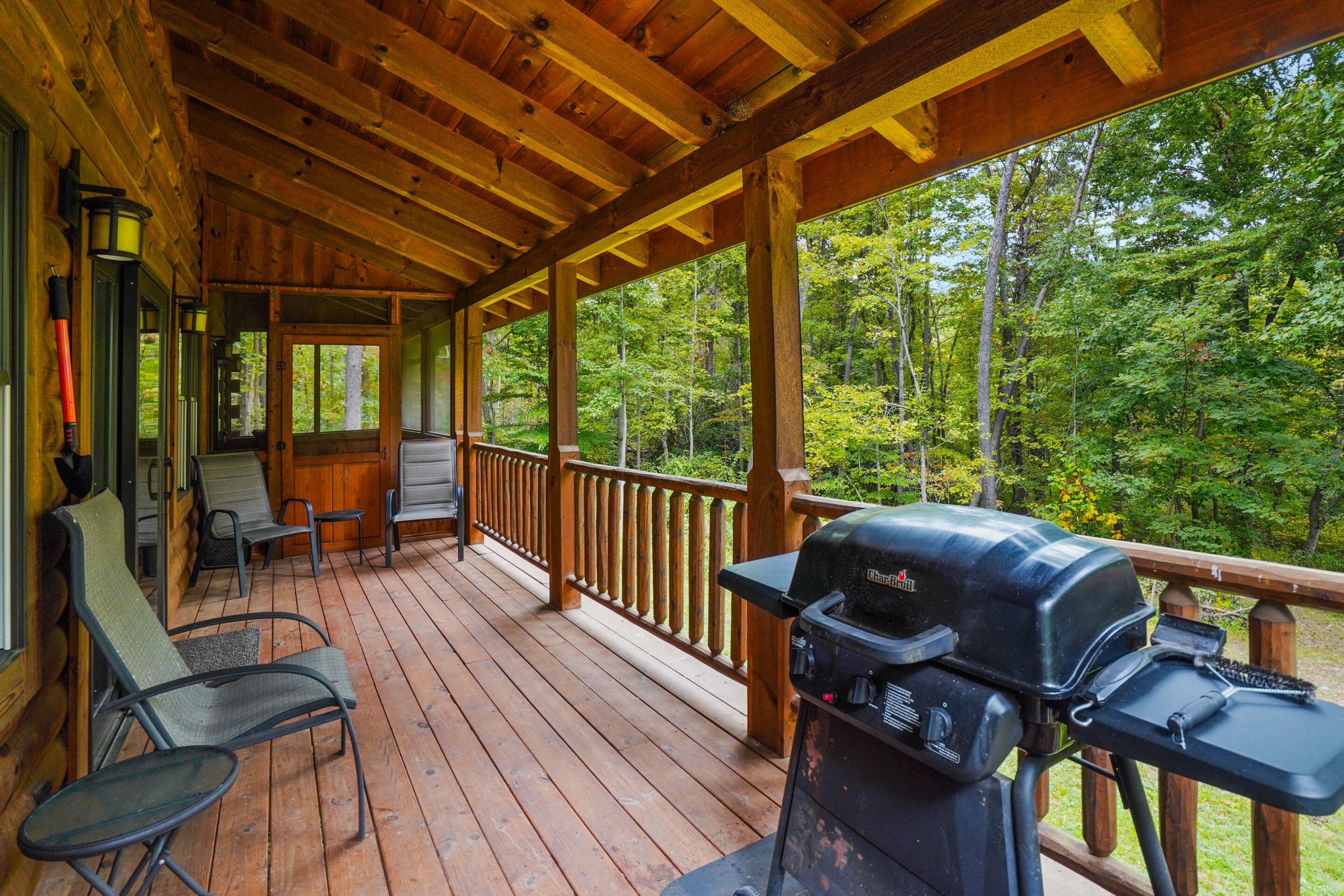 Une terrasse en bois couverte, équipée d’un barbecue, de sièges et offrant une vue sur une forêt.
