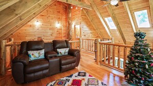 Een gezellige loft slaapkamer met een houten plafond, een leren bank, een kerstboom en uitzicht op de omgeving.