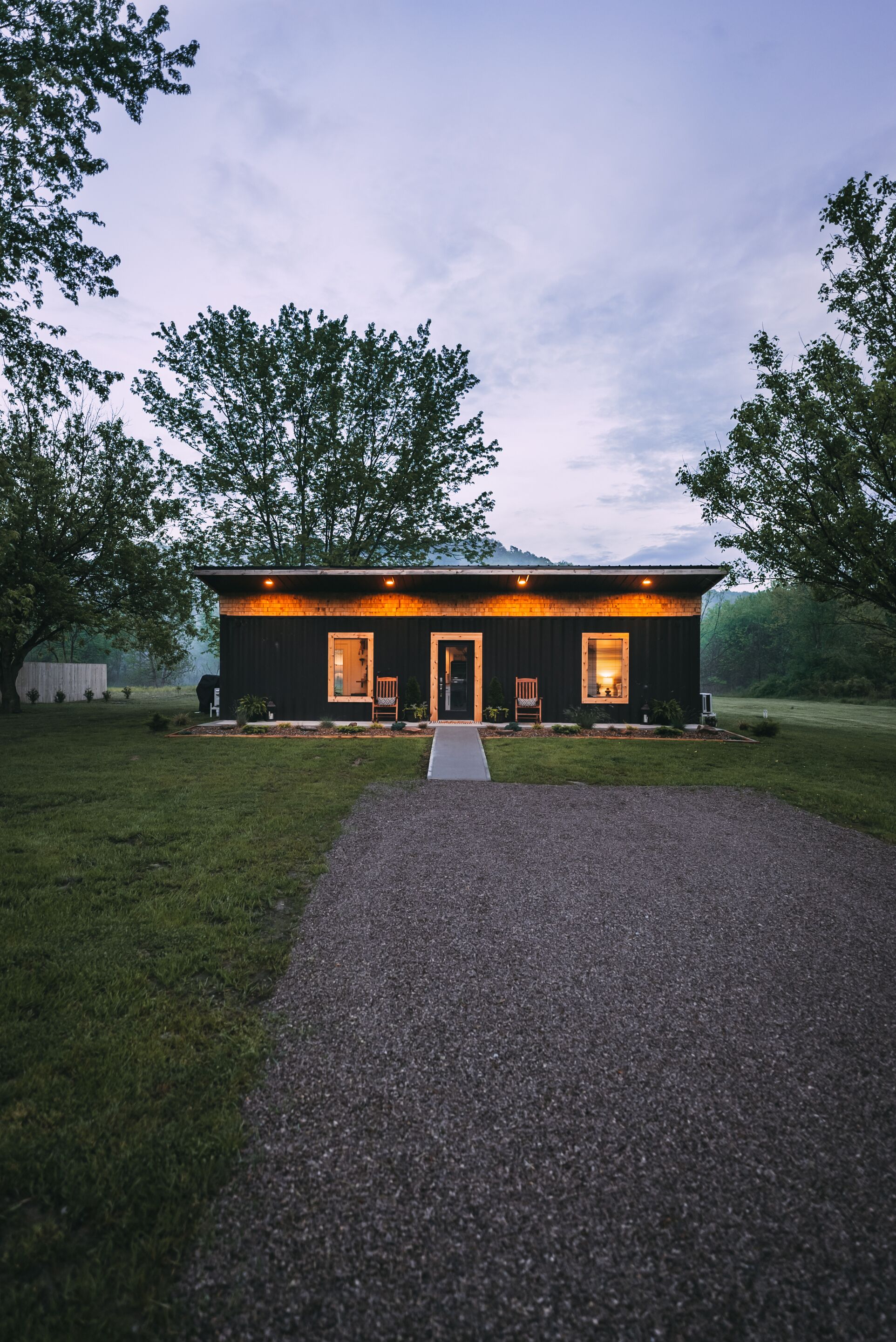 A modern house with a gravel driveway leading to a front door, surrounded by trees.