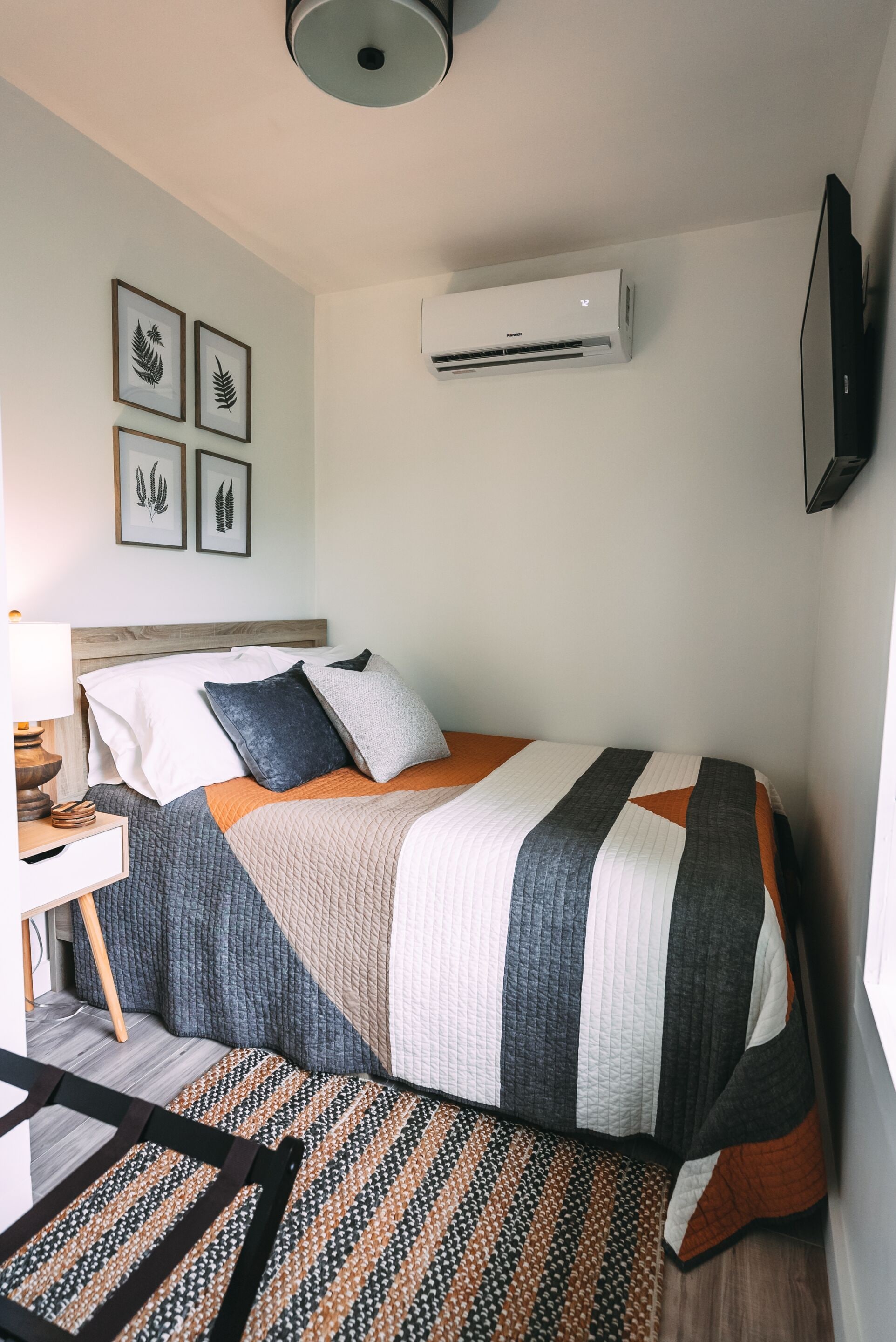 A bedroom with a bed, a bedside table, a lamp, a wall-mounted TV, and framed botanical prints.