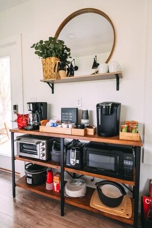Eine Küche mit Kaffeemaschine, Toaster, Mikrowelle und einem Regal mit Pflanze und Tassen.