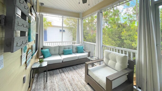 A sunroom with a white ceiling fan, a white sofa with teal cushions, a white armchair, and a view of trees through large windows. -  PARADISE PALMS 6016 at Rookery III - Walk to Beach - Relax by Pools (Gulf Shores)