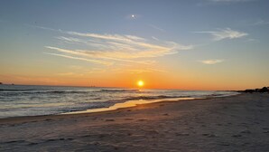 A beach at sunset with a clear sky, ocean waves, and distant buildings. -  PARADISE PALMS 6016 at Rookery III - Walk to Beach - Relax by Pools (Gulf Shores)