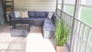 Ein überdachter Patio-Bereich mit einer Eckcouch, einem Korbsessel und einem Blumentopf.