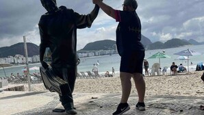 Een standbeeld van een man en een vrouw op een openbaar plein, met een strand en bergen op de achtergrond.