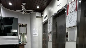 Een net, modern liftgedeelte met roestvrijstalen deuren, een digitaal scherm en een plafondventilator.