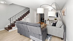 En moderne stue med en grå sofa, en trappe og et spiseområde.