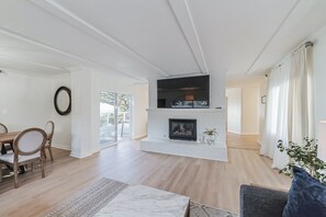 A spacious living room with a fireplace, wooden flooring, and a dining area with a table and chairs. - Oceanview Coastal Retreat Sauna, Hot Tub & Fire Pit
STR Permit Number: 14614430 (Pacifica)