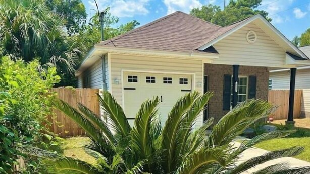 Una casa residencial con garaje, rodeada de exuberante vegetación y una palmera.