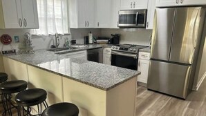 Una cocina moderna con armarios blancos, electrodomésticos de acero inoxidable, encimera de granito y taburetes de bar negros.
