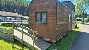 A small wooden cabin with a ramp leading to the entrance, situated next to a paved path. - Tiny Haus Tinyhouse Waldcamping Prüm Eifel (Prüm)