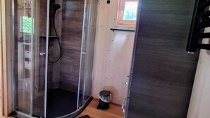 A wooden cabin interior with a glass shower enclosure, a small window, and a door leading to another room. - Tiny Haus Tinyhouse Waldcamping Prüm Eifel (Prüm)