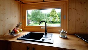 A kitchen with a wooden countertop, a black sink, a window with a view of greenery, and a fruit bowl. - Tiny Haus Tinyhouse Waldcamping Prüm Eifel (Prüm)