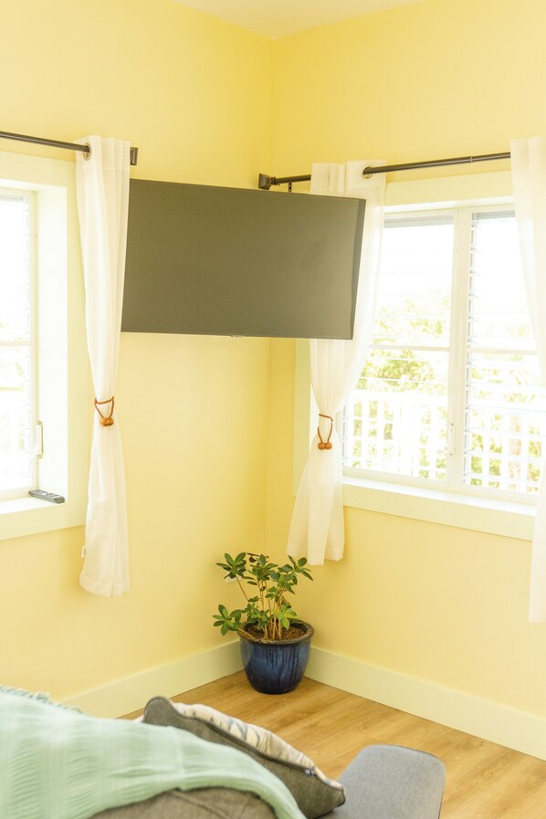 A room with a bed, a potted plant, and a window with curtains.