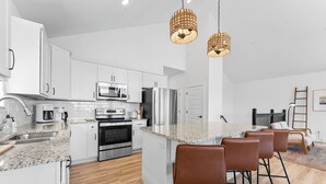 A modern kitchen with white cabinets, stainless steel appliances, a granite countertop, and a bar area with stools.