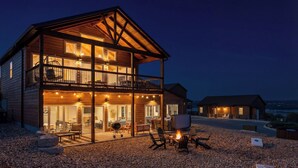 A two-story wooden house with a balcony, outdoor seating, and a fire pit.