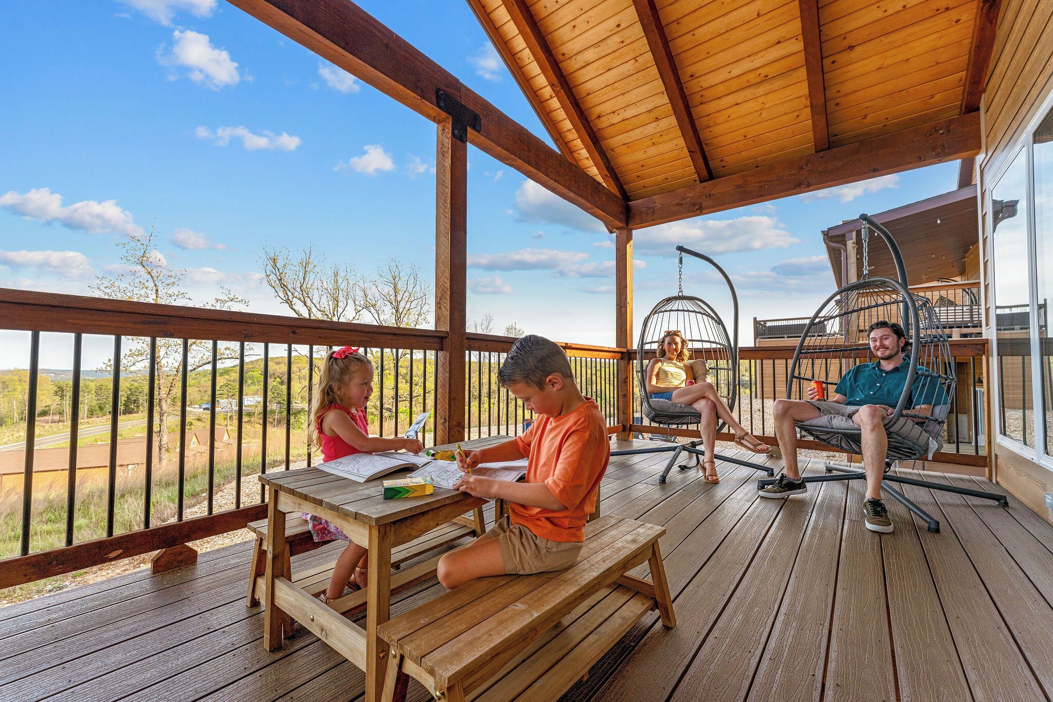 Una terraza de madera con zona cubierta, una mecedora y una mesa de comedor.