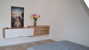 Une chambre à coucher avec un lit, une commode en bois, un téléviseur fixé au mur et un tableau.