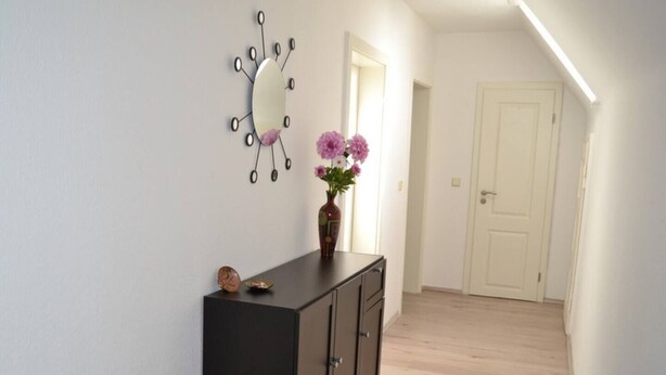 Un couloir avec une commode en bois foncé, un miroir décoratif et un vase rempli de fleurs.