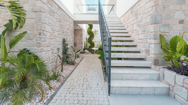A modern staircase with stone walls and a metal railing, surrounded by potted plants and a paved pathway. - Bodrum Local House (Bodrum)