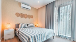 A modern bedroom with a large bed, bedside lamps, a wall-mounted air conditioner, and a view of trees through sheer curtains. - Bodrum Local House (Bodrum)