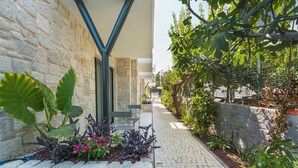 A stone wall with a metal structure, a paved pathway, and various plants. - Bodrum Local House (Bodrum)