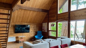 Un interior acogedor de cabaña con un sofá modular, una mesa de comedor y un televisor montado en la pared.