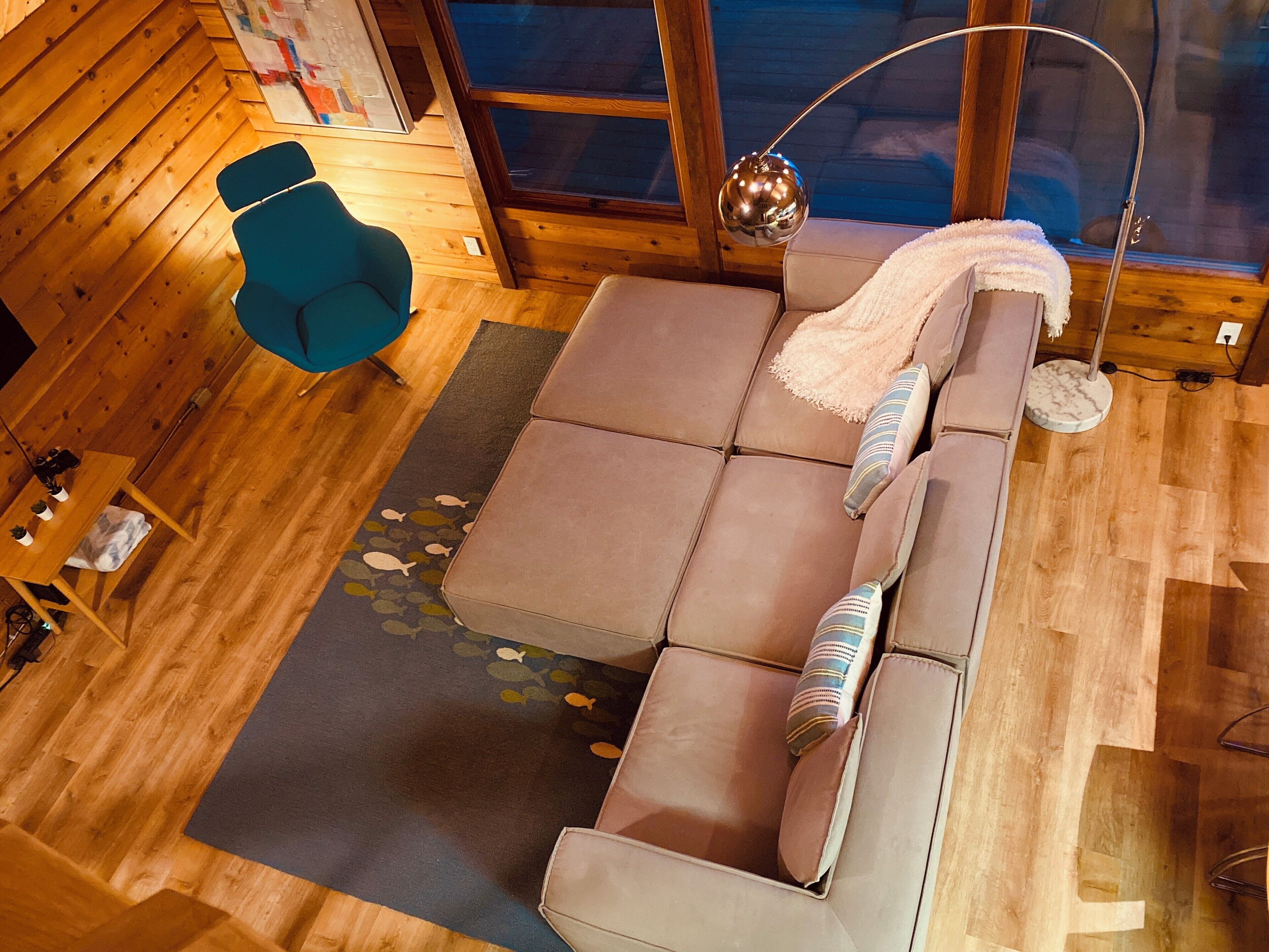 Ein gemütliches Zimmer mit einer Eckcouch, einem blauen Sessel, einer runden Lampe und Holzboden.