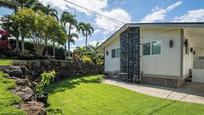 Una casa moderna con un muro de contención de piedra, un césped cuidado y una zona de patio con mobiliario exterior.
