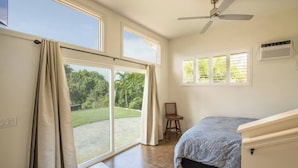 Un dormitorio con cama, ventilador de techo y vista a un jardín por una puerta corrediza.