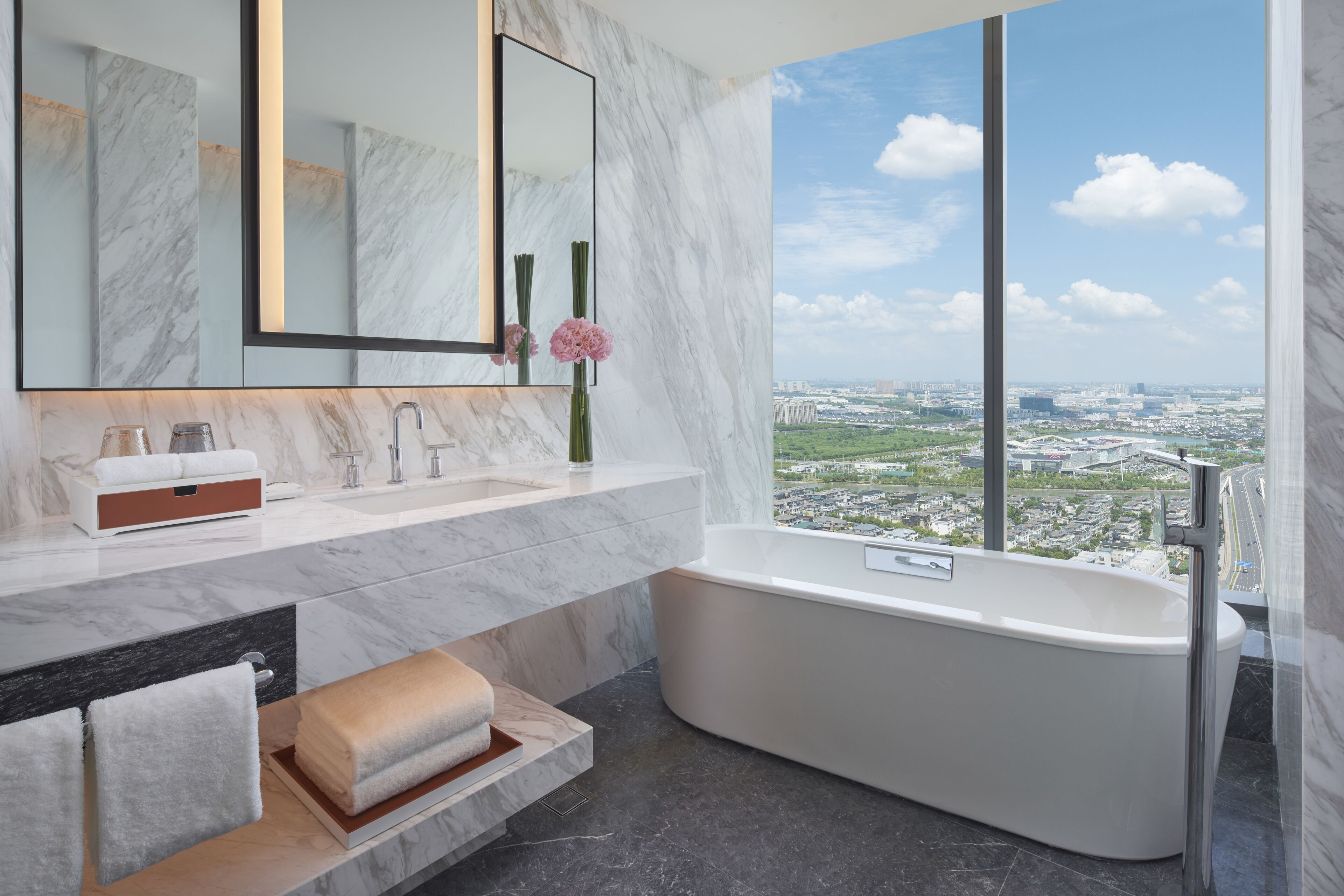 A modern bathroom with a large bathtub, a marble vanity, a large mirror, and a view of a cityscape.