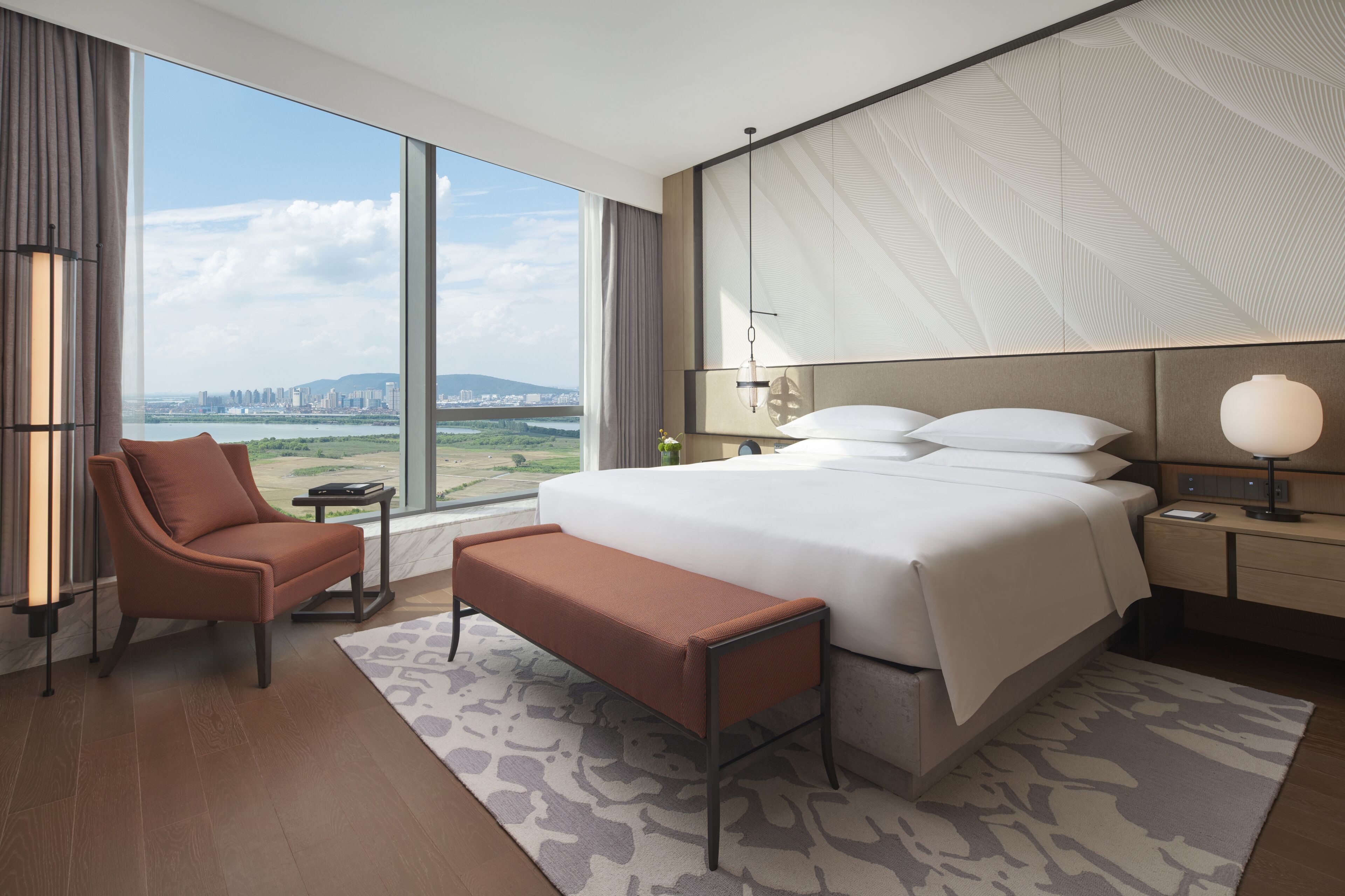 Een moderne hotelkamer met een groot bed, een zithoek, een bureau en uitzicht op een stadsgezicht.