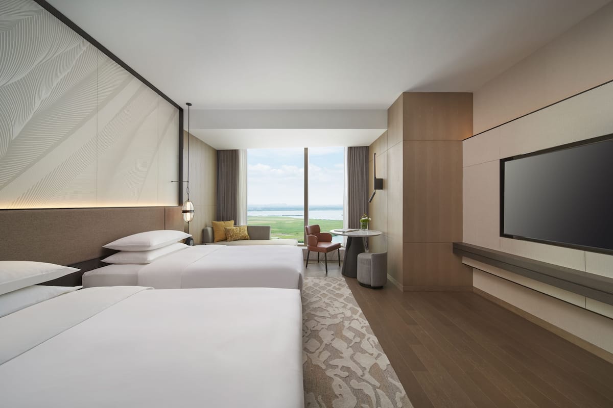 Une chambre d’hôtel avec deux lits, une télévision, un bureau et une vue sur l’extérieur.