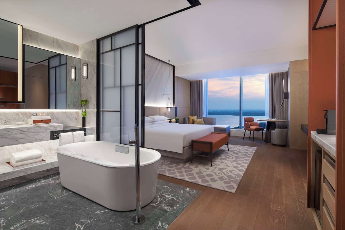Une chambre d’hôtel moderne dotée d’un grand lit, d’un coin salon séparé, d’une salle de bain avec baignoire et d’une vue sur l’océan.