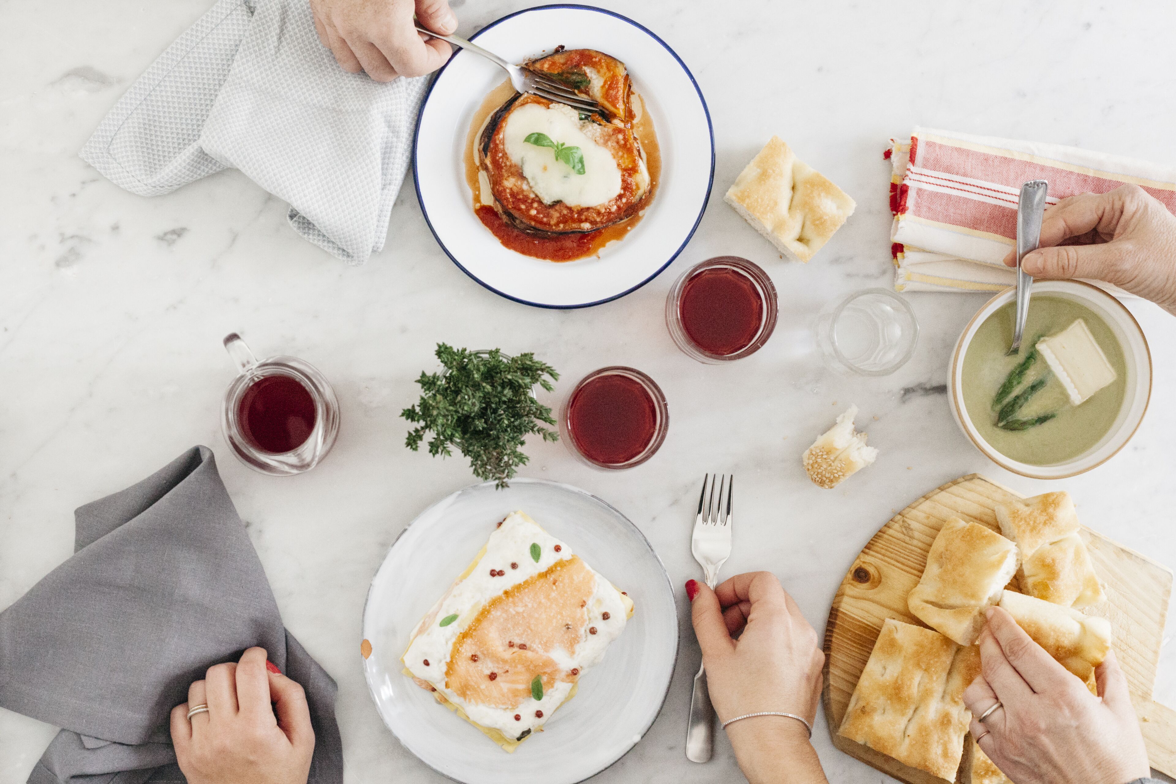 Une table à manger avec différents plats, notamment une assiette de lasagnes, un bol de soupe et une assiette de pain.