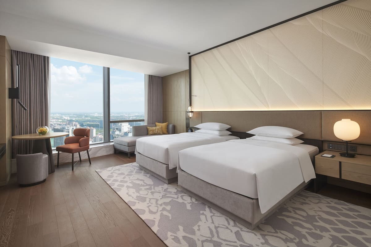 Une chambre d’hôtel moderne avec deux lits, un petit coin salon et une grande fenêtre donnant sur la ville.