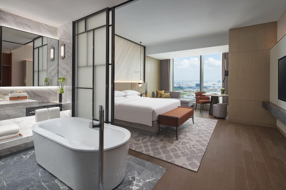 Une chambre d’hôtel moderne dotée d’une grande baignoire, d’un lit, d’un coin salon et offrant une vue sur la ville.