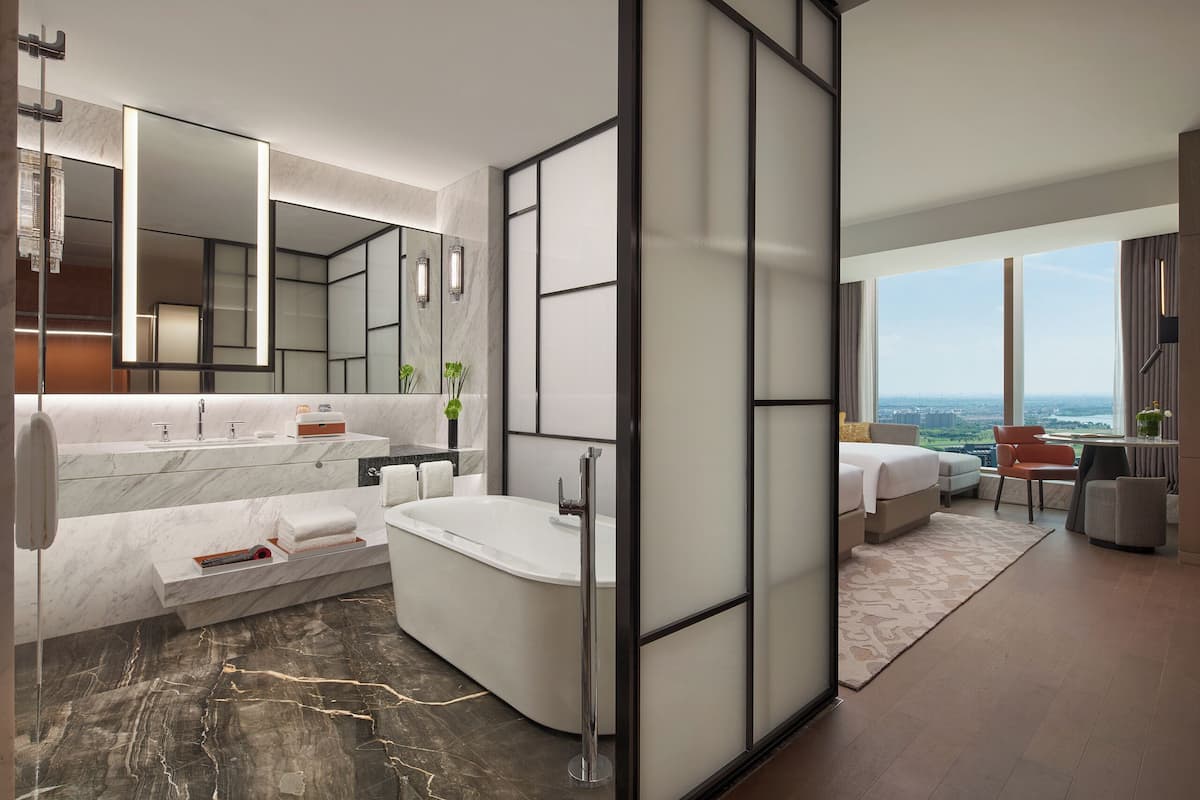 Une salle de bain d’hôtel moderne, dotée d’une baignoire, d’un grand miroir et d’un meuble-lavabo avec un plan de travail en marbre.