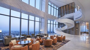 A spacious lobby with a large seating area, a spiral staircase, and large windows offering a city view. - Hyatt Regency Changshu Kuncheng Lake (Suzhou)