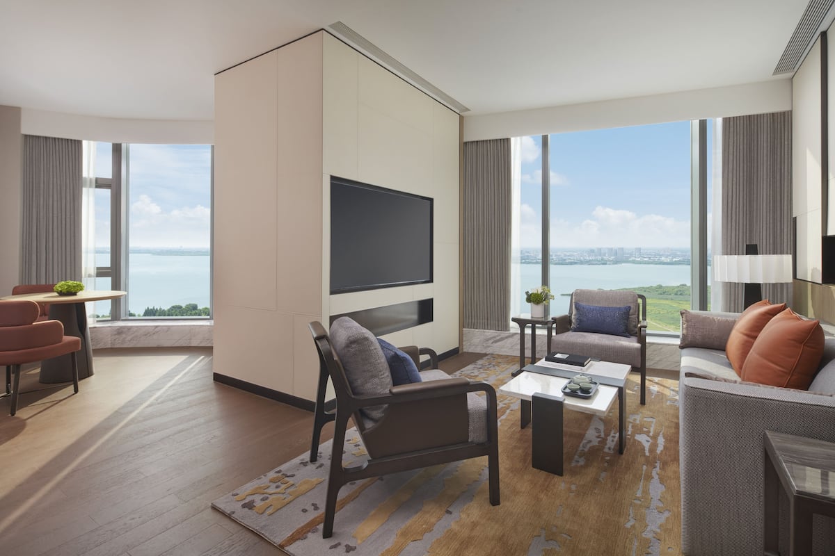 Une chambre d’hôtel moderne dotée d’une grande télévision à écran plat, de sièges confortables, d’un coin repas et offrant une vue sur la ville et l’eau.