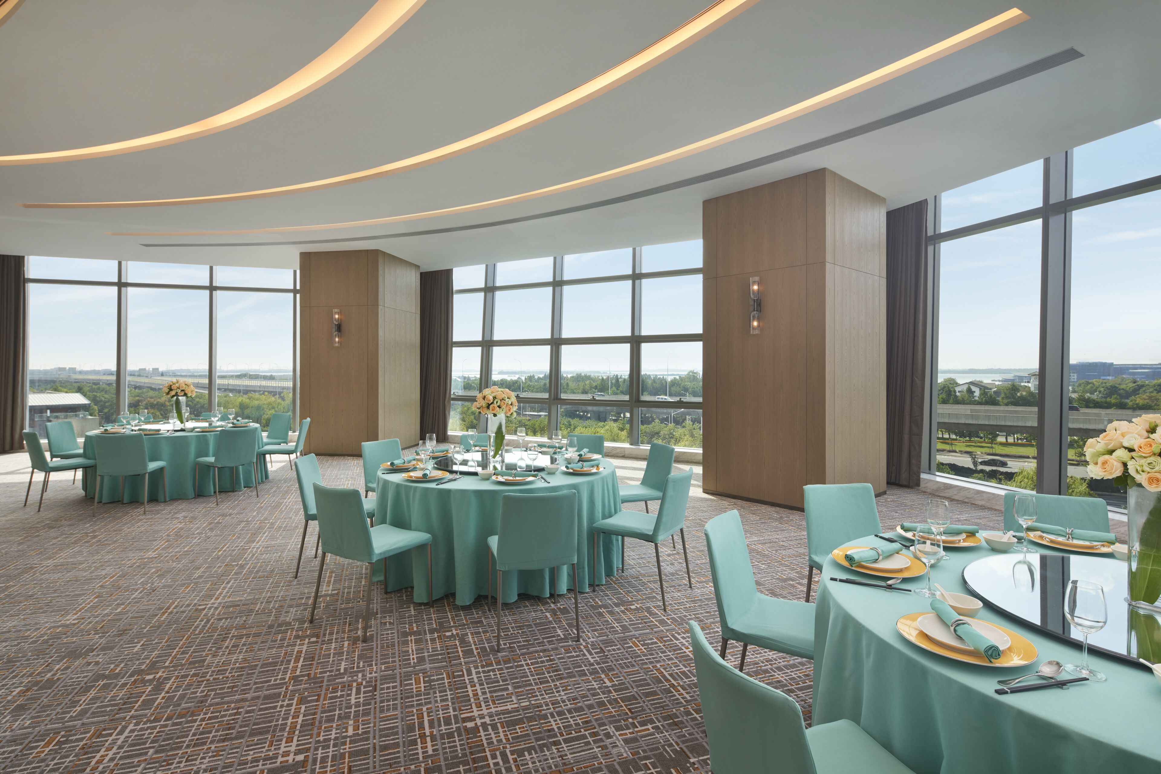 A spacious dining area with round tables, teal chairs, and a panoramic view through large windows.