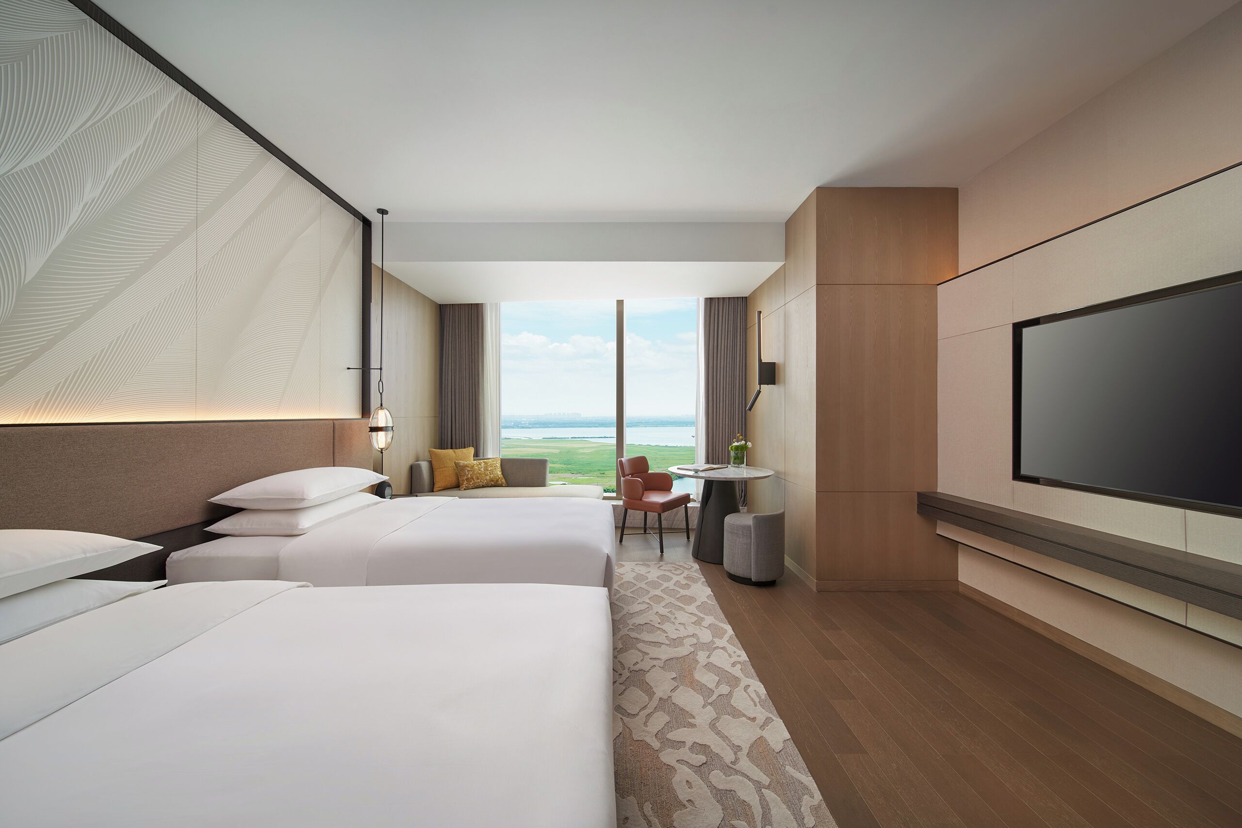 A hotel room with two beds, a TV, a desk, and a view of the outdoors.