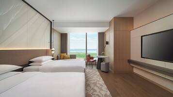 A hotel room with two beds, a TV, a desk, and a view of the outdoors.