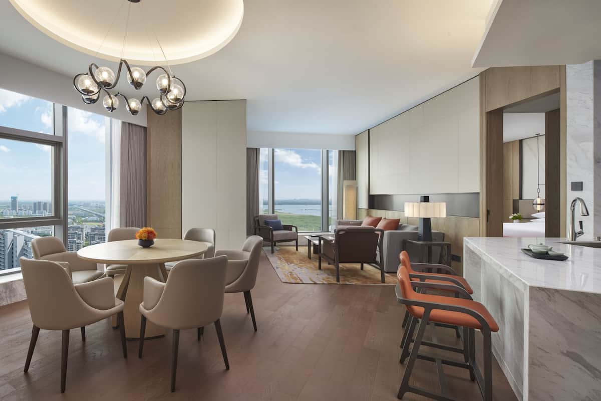 Une chambre d’hôtel moderne dotée d’un coin repas, d’une cuisine et d’une grande fenêtre donnant sur la ville.