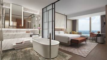 Relax in a spacious room with a bathtub, separate sitting area, and city views from the large windows.
