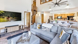 A modern living room with a large flat-screen TV, a grey sofa, and a staircase leading to an upper level. - Ski In/out with HOT TUB! PENTHOUSE, Walk to Ski School & Restaurants! BC Village (Beaver Creek)