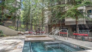 An outdoor swimming pool with a metal ladder, surrounded by a metal fence and trees. - Charlie's Slopeside: Ski-In/Out Penthouse, Creekside, Sleeps 7, Hot Tub, Walk to Ski School (Beaver Creek)